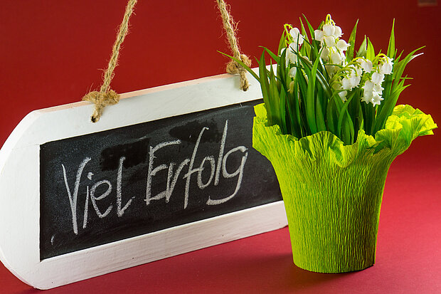 Tafel mit der Aufschrift "Viel Erfolg" und eine kleine Blume als Präsent.