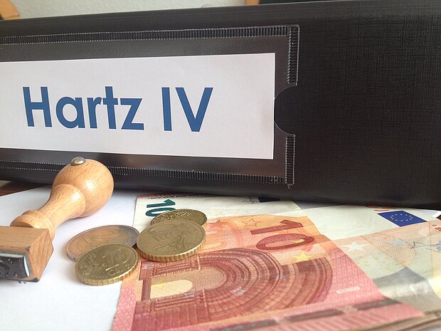 Ordner mit der Aufschrift "Hartz IV", einem Stempel davor und Euro-Münzen sowie Geldscheine