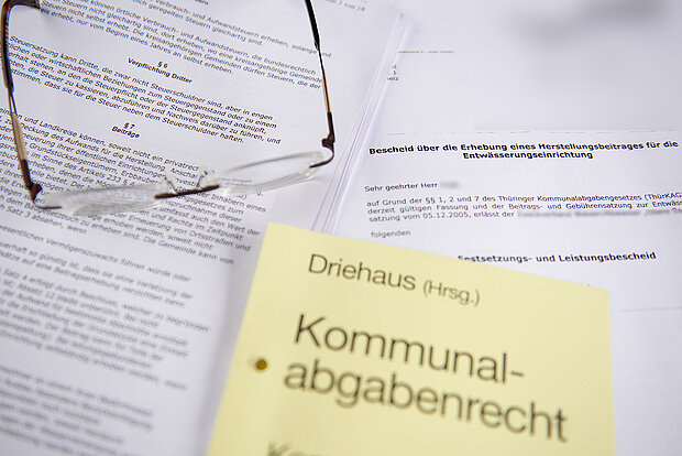 eine Brille und ein Notizzettel mit der Aufschrift "Kommunalabgabenrecht" liegen auf Dokumenten