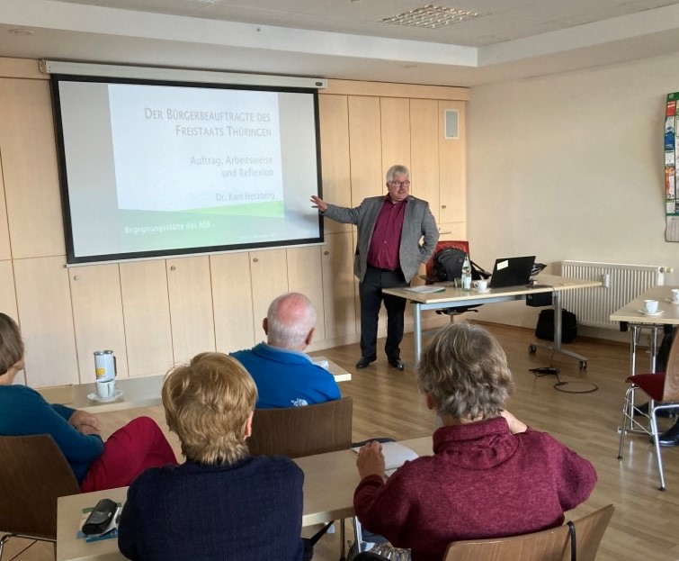 Dr. Herzberg mit Powerpoint einen Vortrag vor Zuschauern haltend